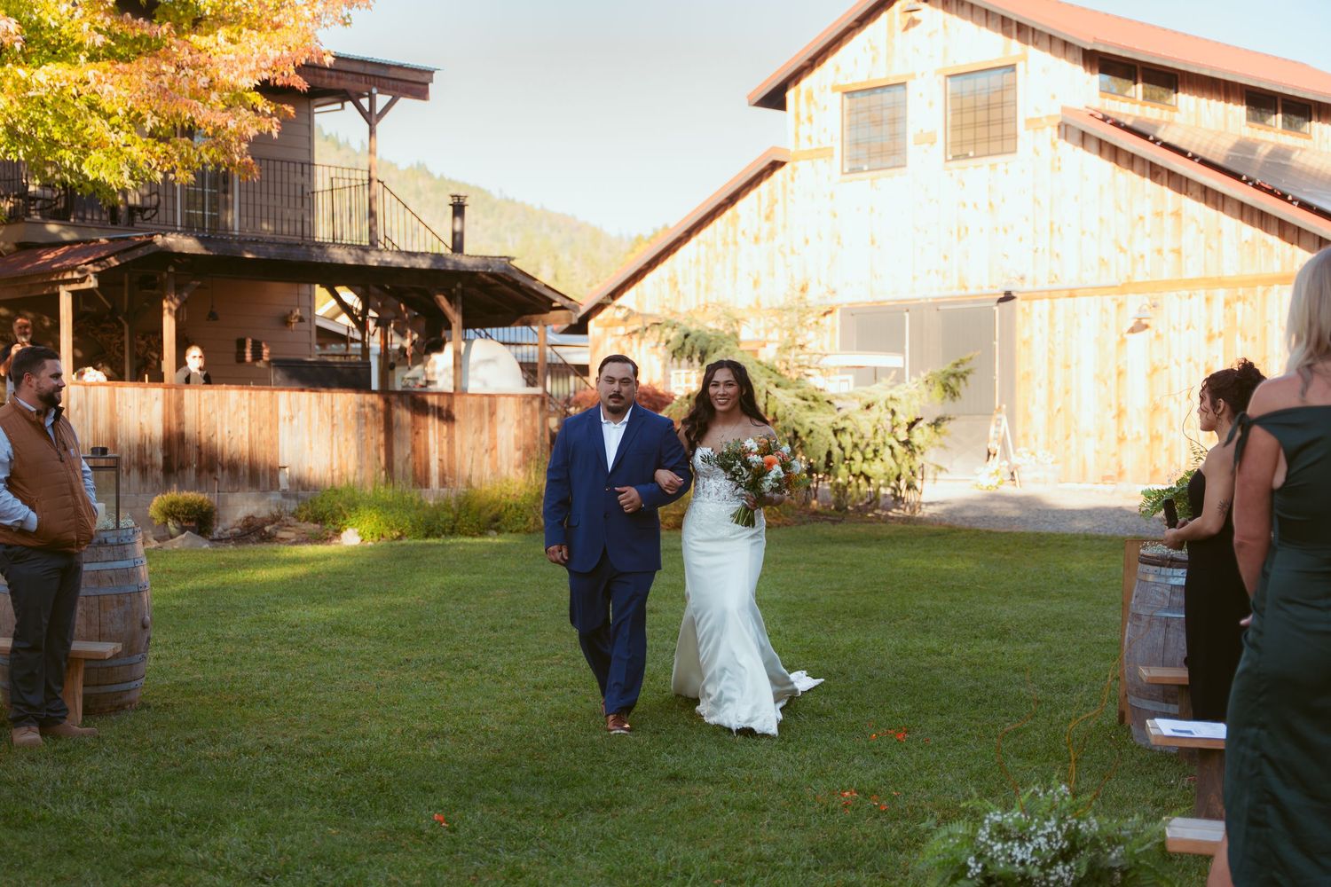Wedding ceremony procession walking across a green lawn with a barn in the background.