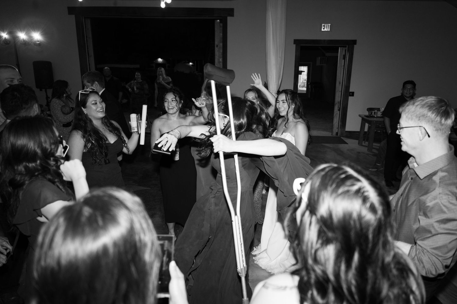Black and white image of people dancing with illuminated glow sticks at an indoor event.
