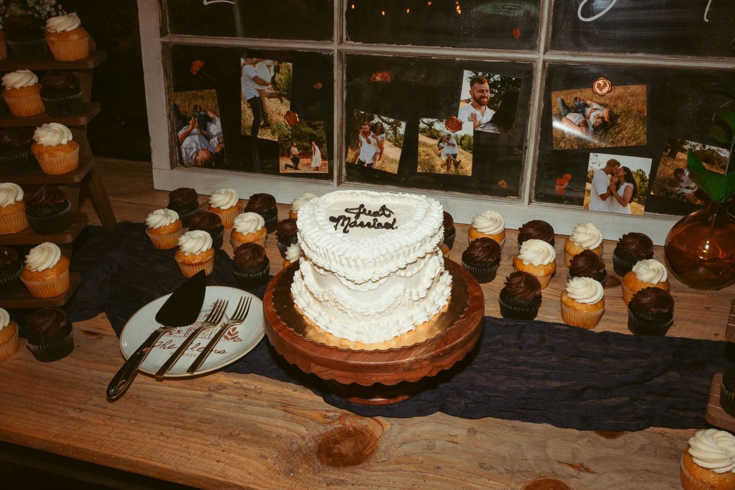 White wedding cake displayed on dark wooden table surrounded by small candles in mason jars.