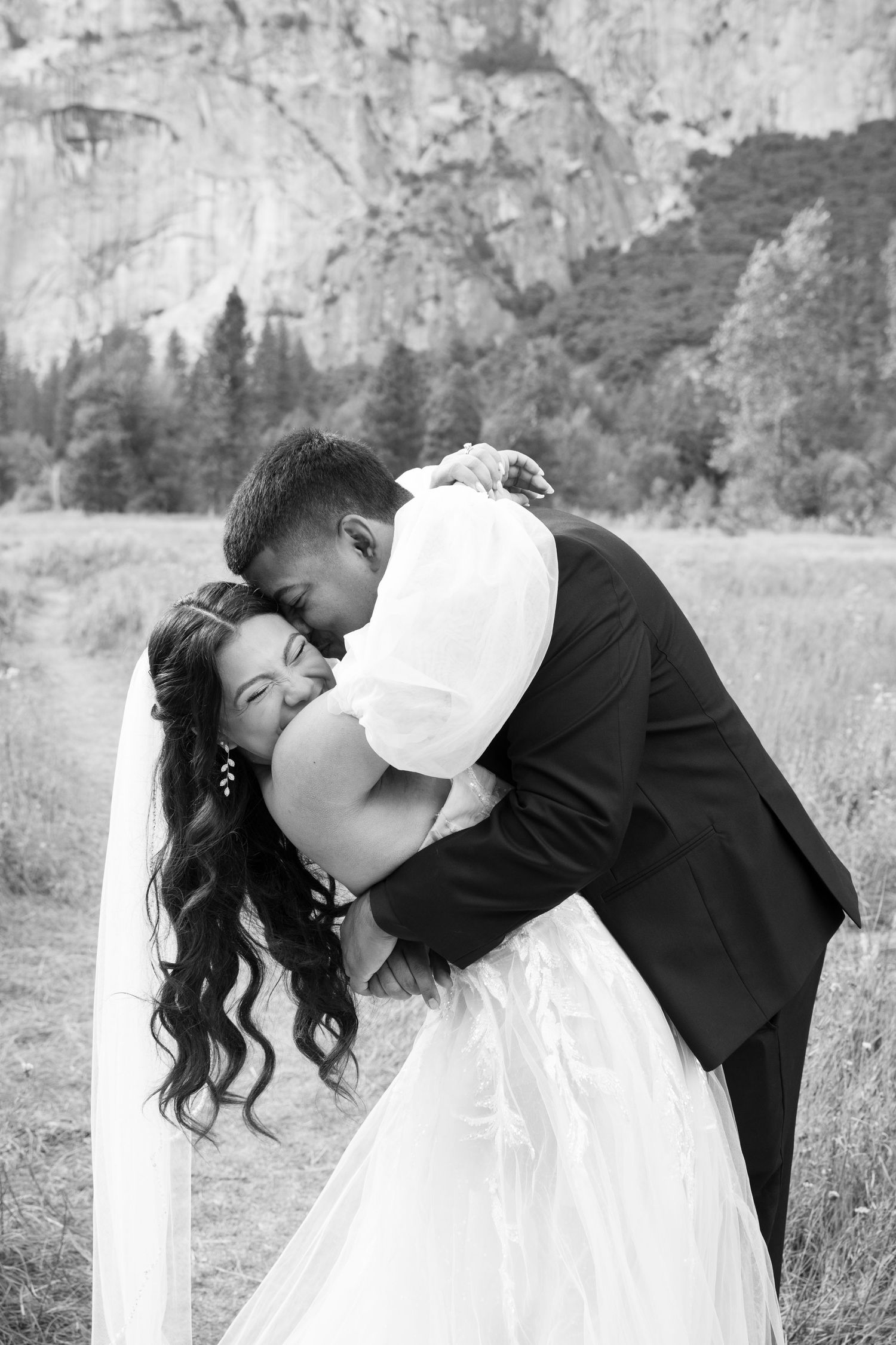 Black and white photo of a couple sharing their first kiss as newlyweds against a mountain backdrop.
