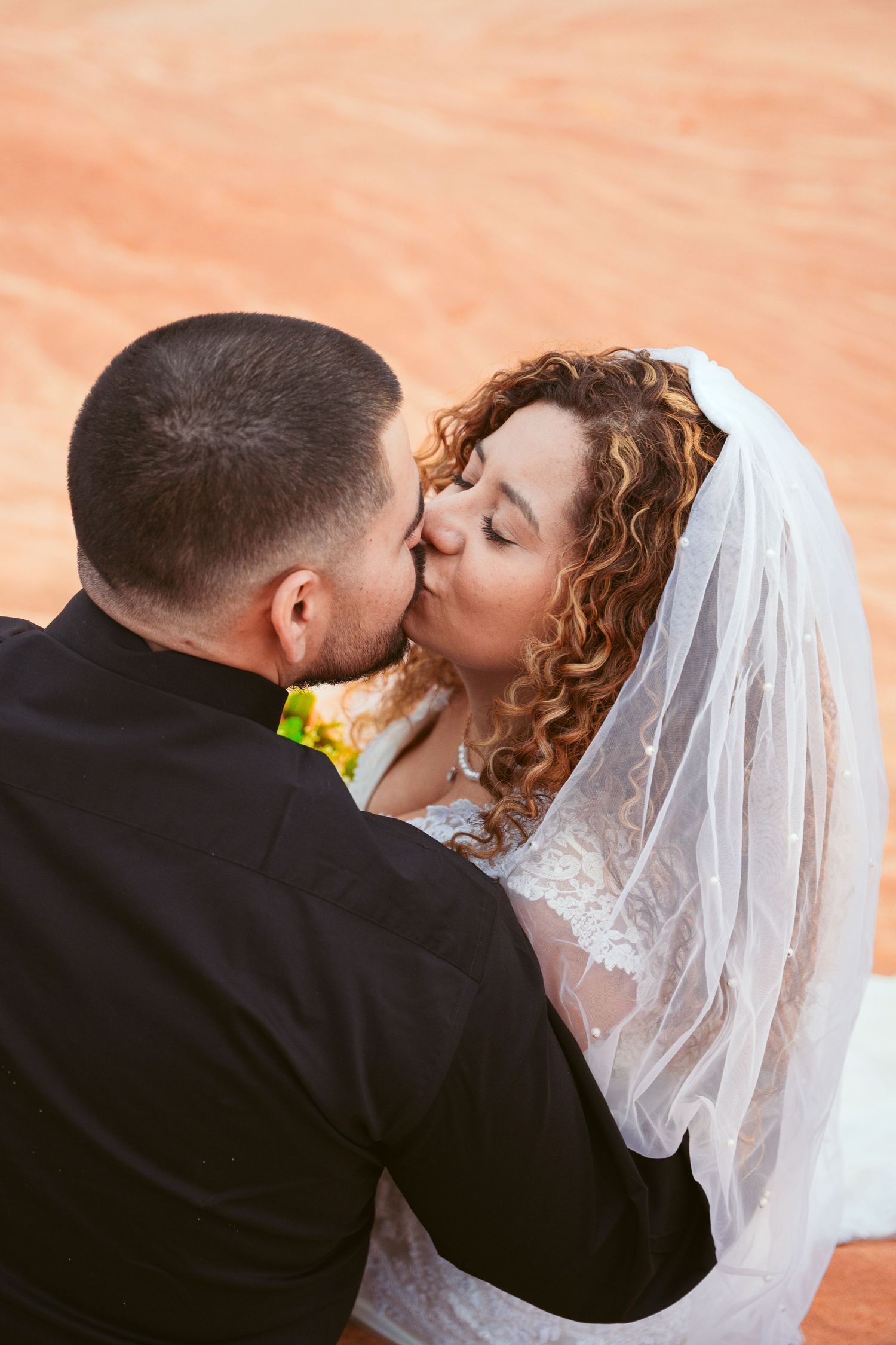 Close-up of newlyweds sharing an intimate kiss against a peach-colored background.