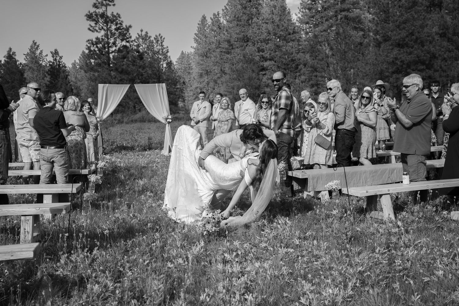 Black and white capture of outdoor wedding celebration with rustic wooden benches.