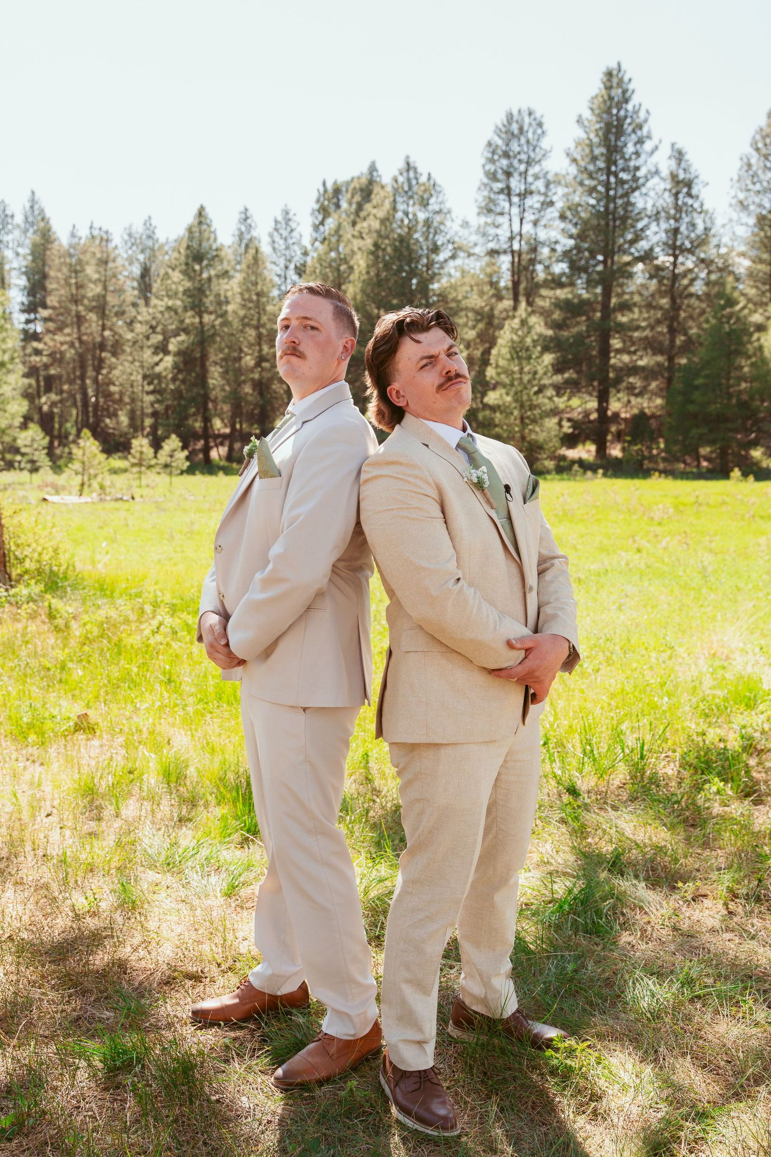 Wedding party members in beige suits strike fun poses in a sunny outdoor setting.