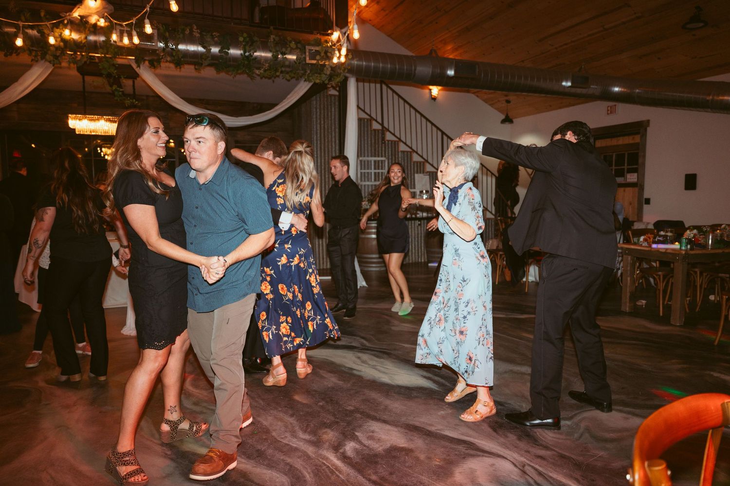 People dancing and socializing under warm string lights at a dimly lit indoor celebration.