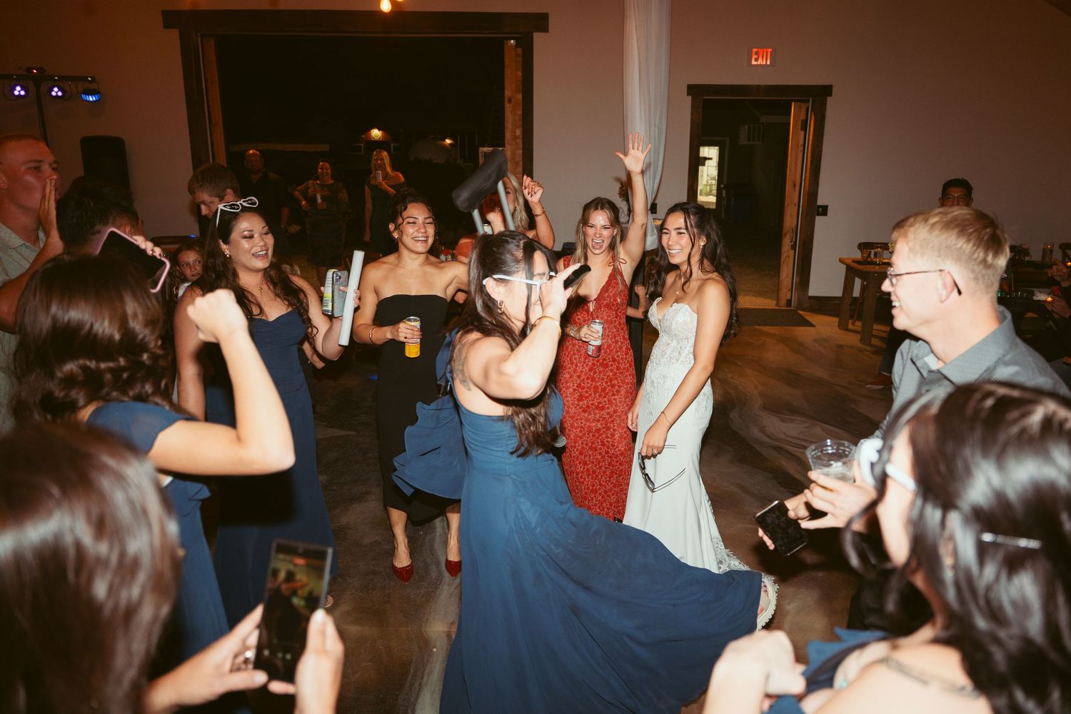 Party guests in formal attire dance and hold up glowing sticks during celebration.