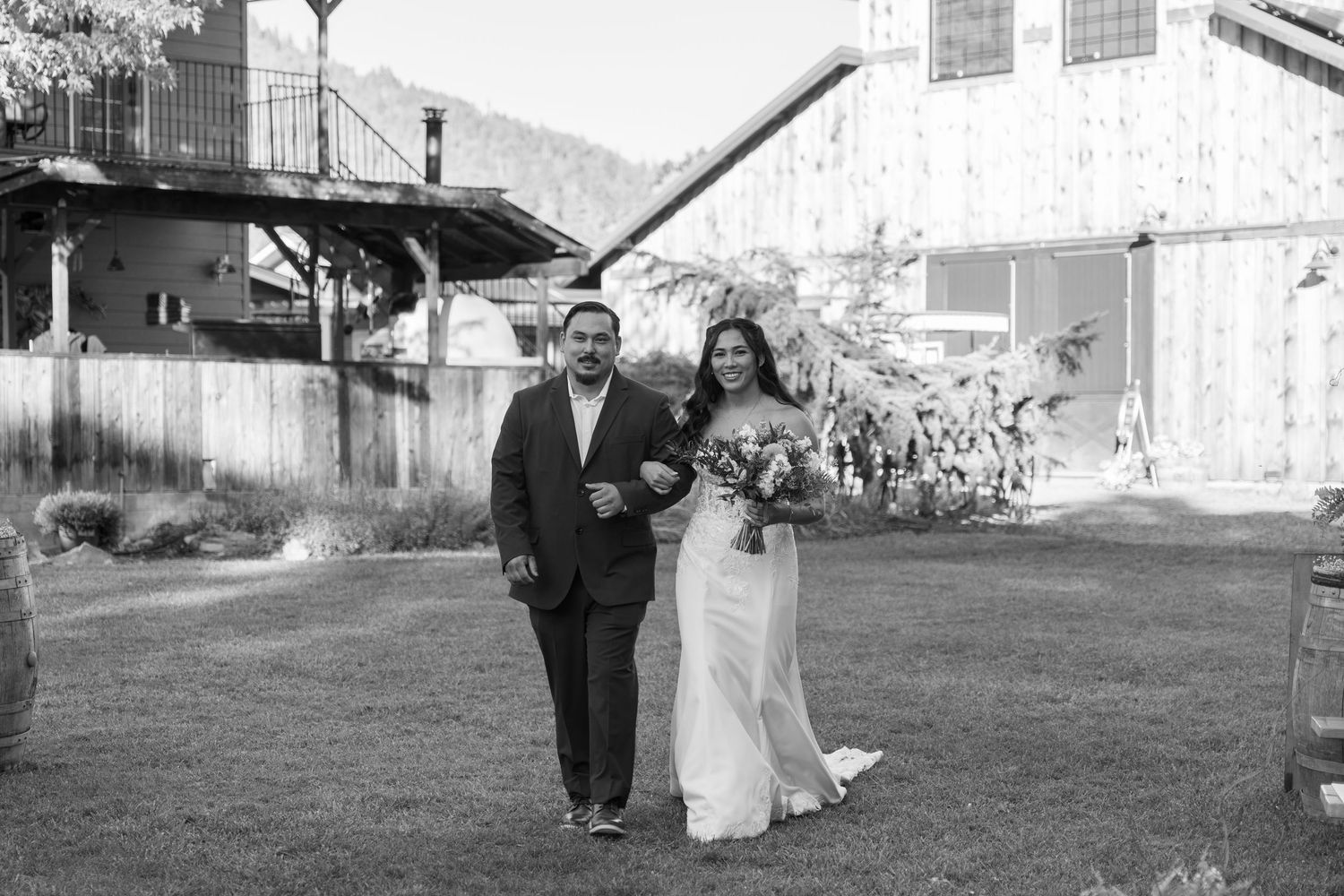 Wedding party walking on a grassy lawn in front of a rustic barn during golden hour.