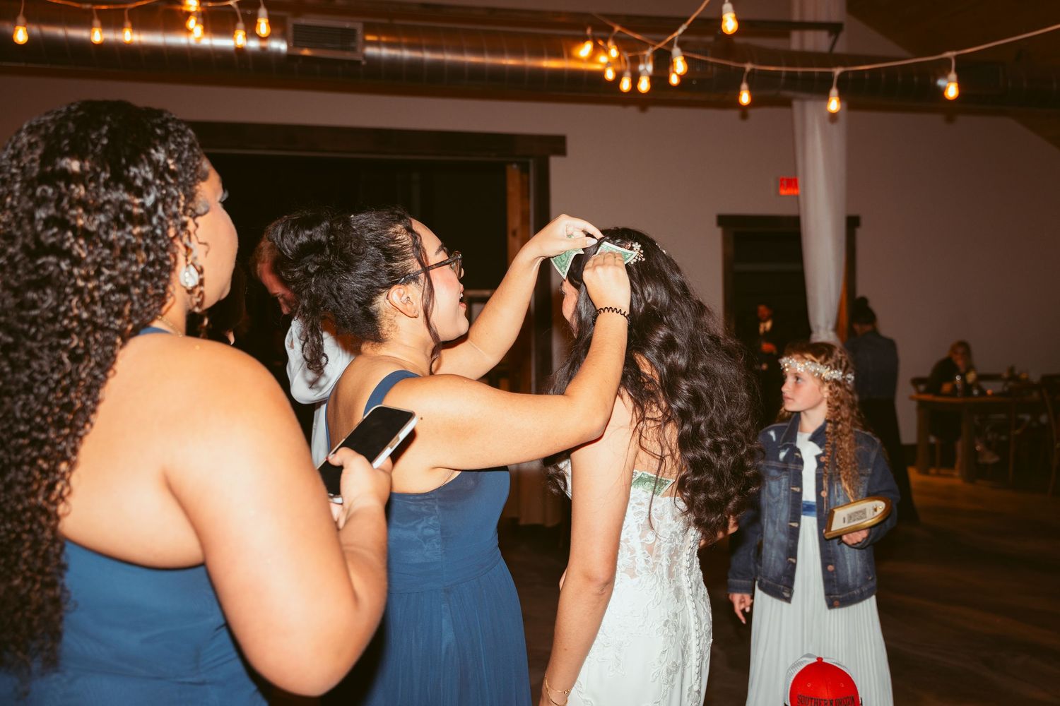 Wedding party members dancing in formal attire under string lights.