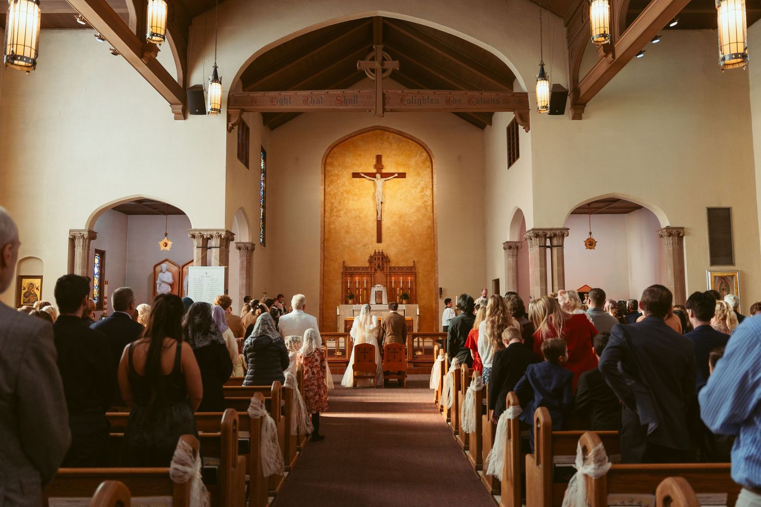 Traditional church wedding ceremony in progress with guests seated in wooden pews under vaulted ceiling.