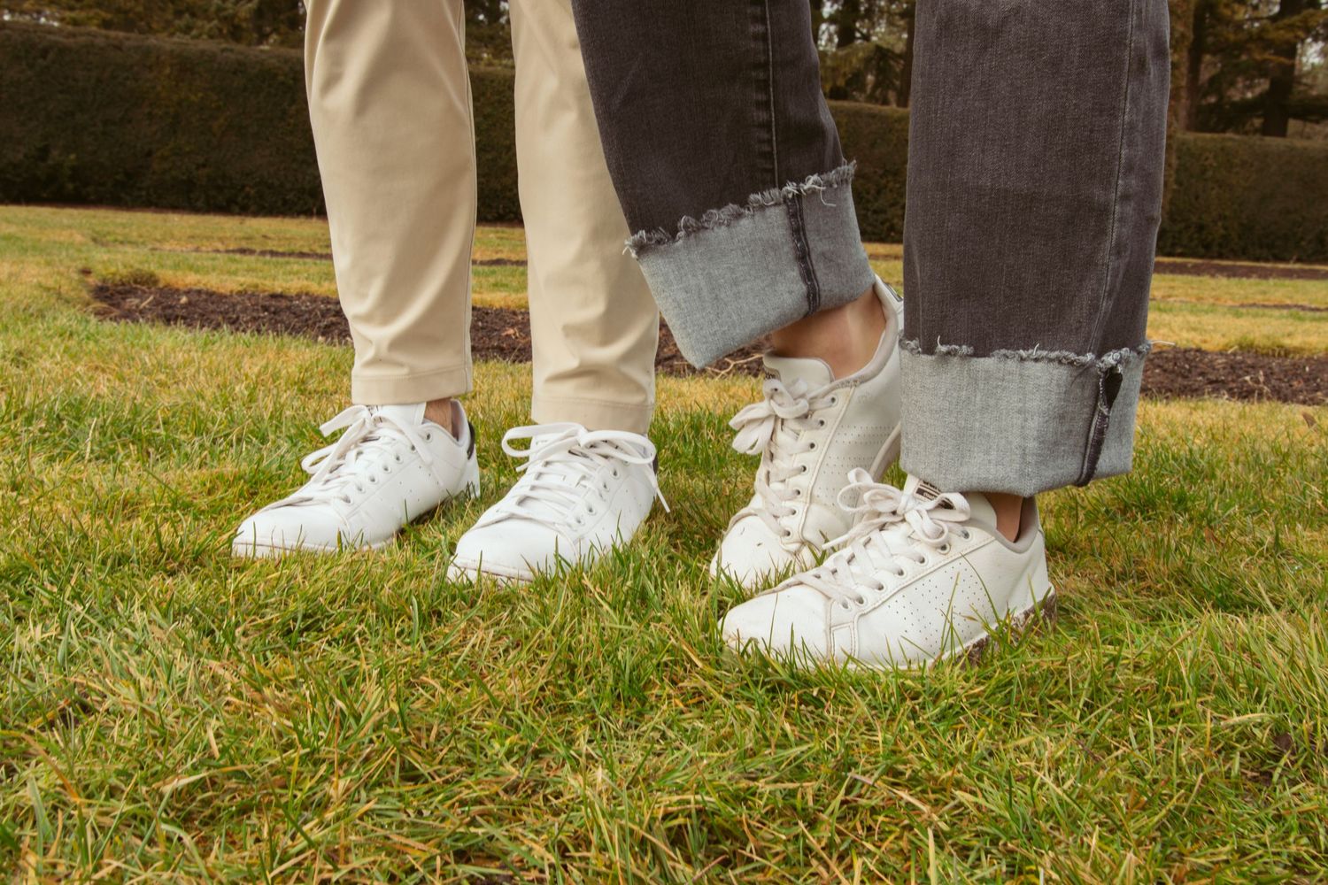 Close-up of matching white sneakers on grass showing coordinated couple's footwear.