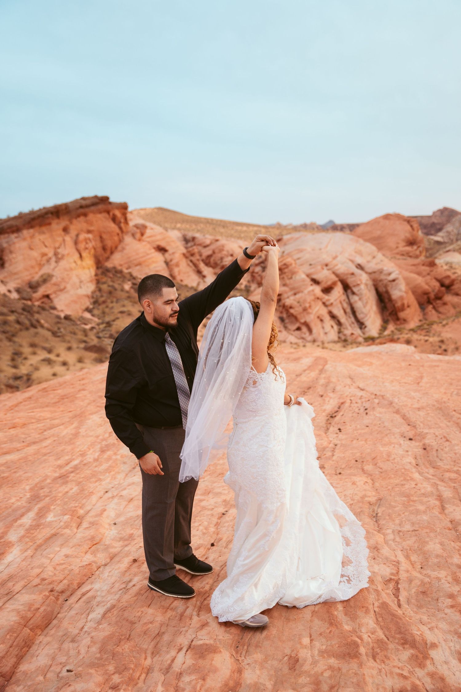 Newlyweds share romantic moments while posing on dramatic red rock formations in the desert.