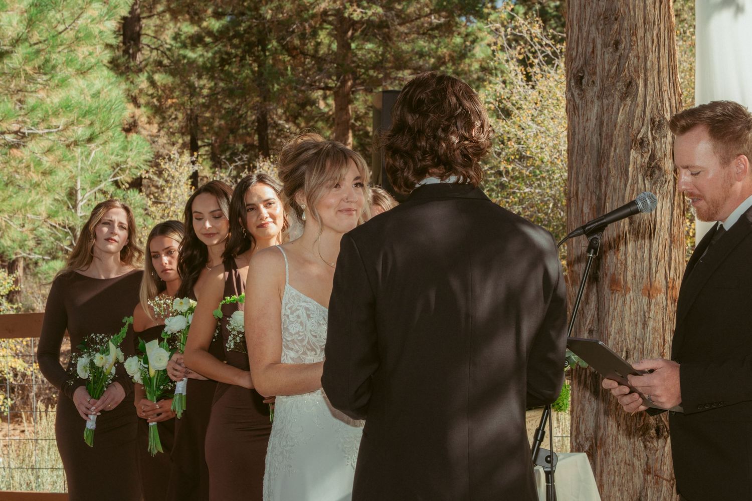 Wedding party stands in formation during forest ceremony with decorative white backdrop.