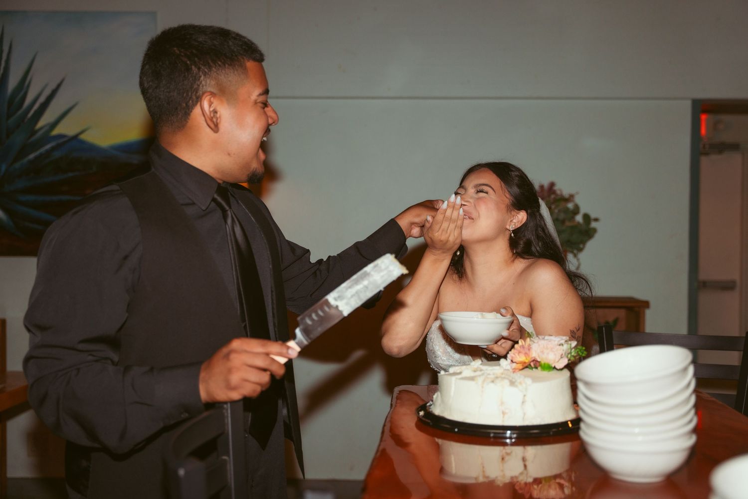 Wedding couple sharing a fun cake-cutting moment at their reception.