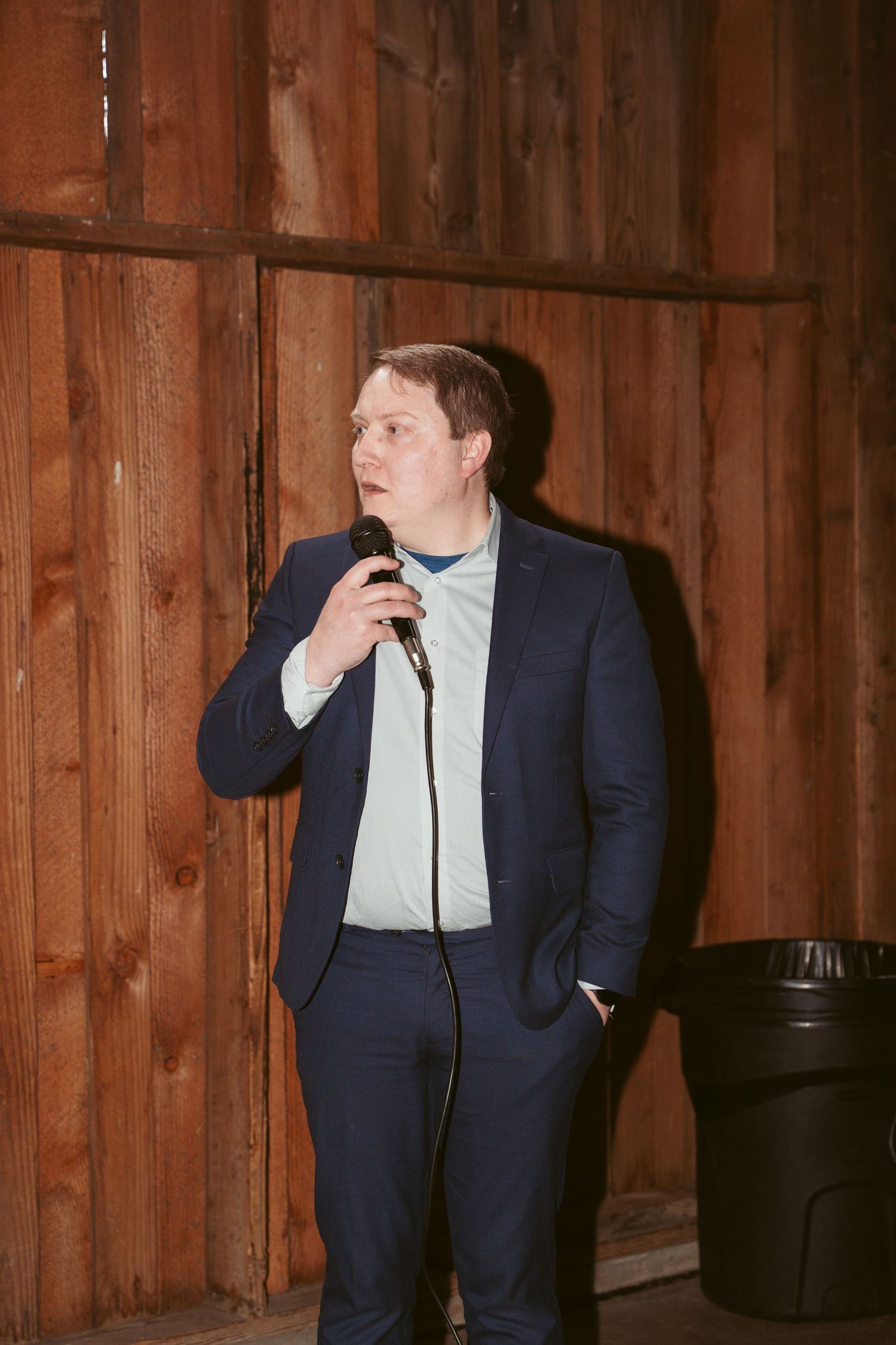 Person in navy suit making expressive gestures during celebration in rustic barn venue.