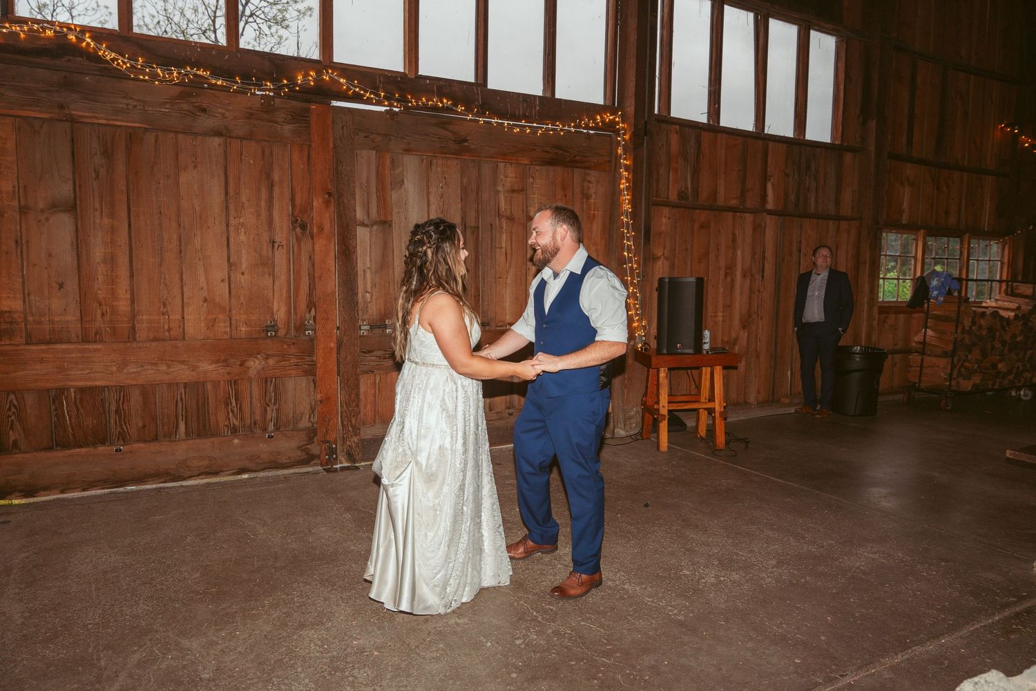 A couple dances in a rustic barn venue with wooden walls and string lights overhead.