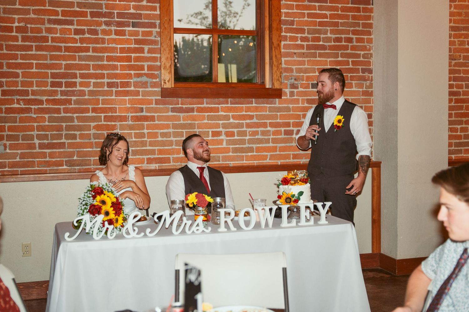 Wedding reception setup in industrial-style venue with brick walls and decorative signage.