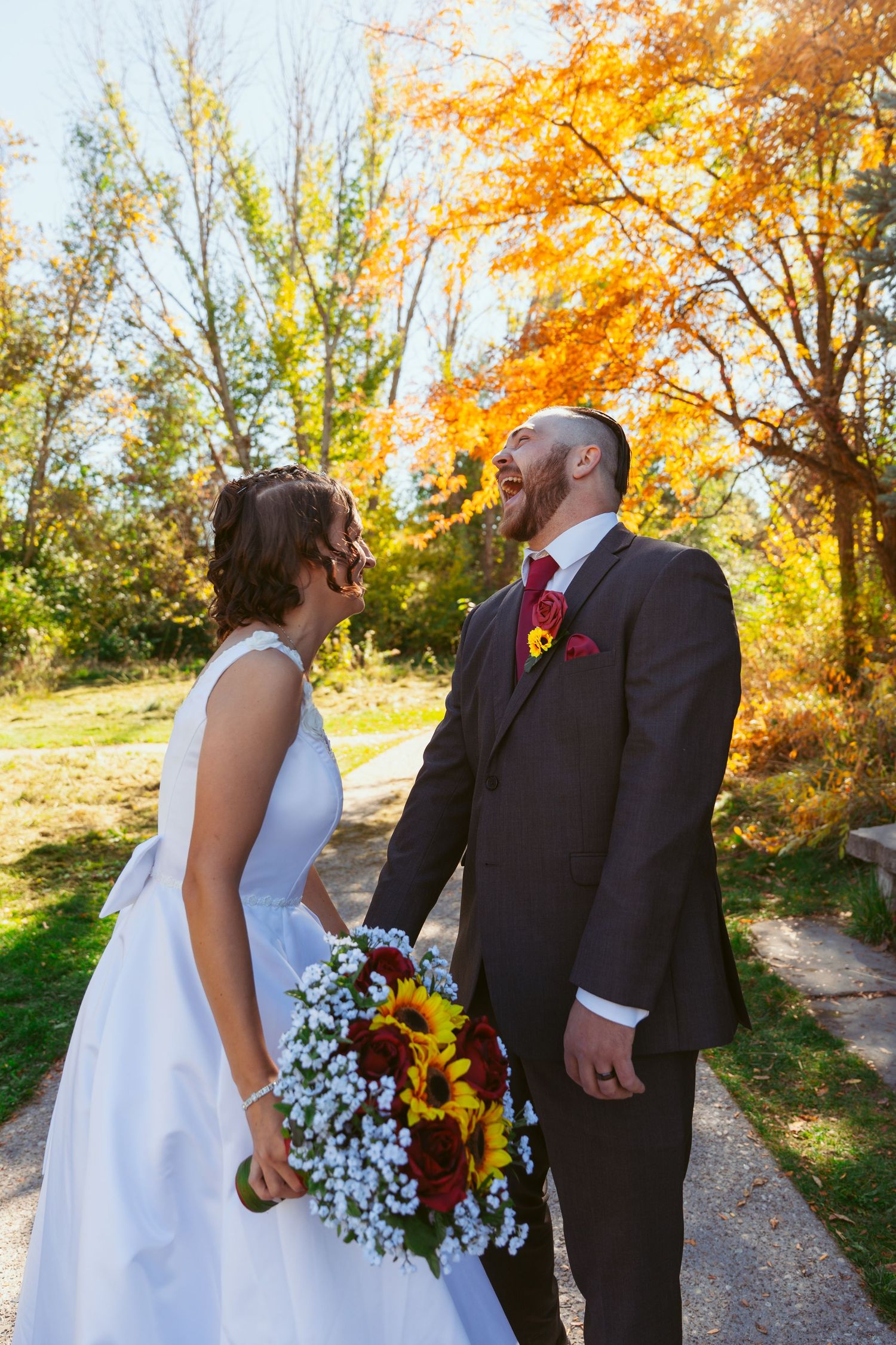 A couple walks hand in hand on a path with sunflowers and autumn colors surrounding them.