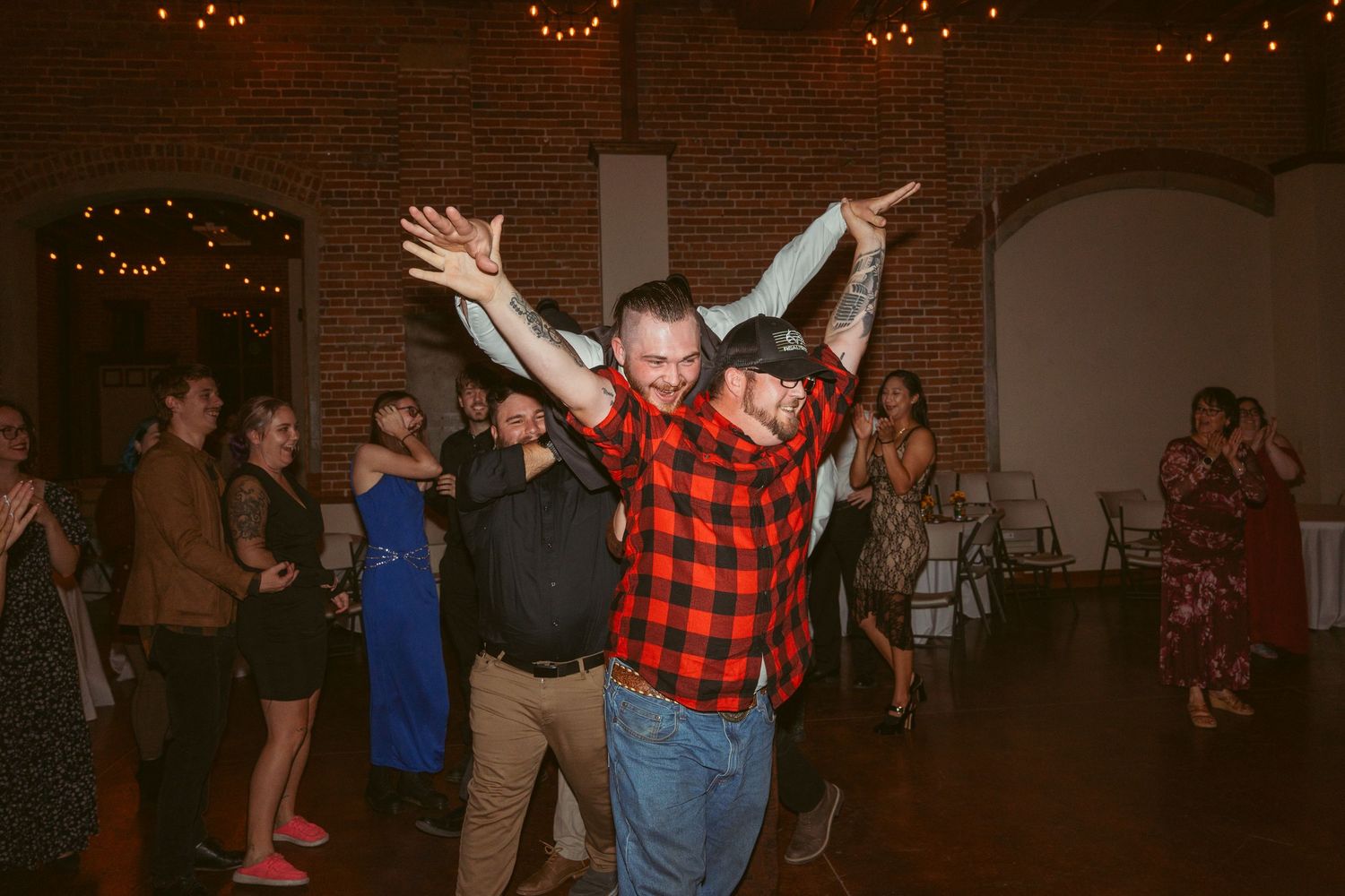 Dancers celebrating with energetic moves on a dance floor decorated with string lights in a brick-walled venue.