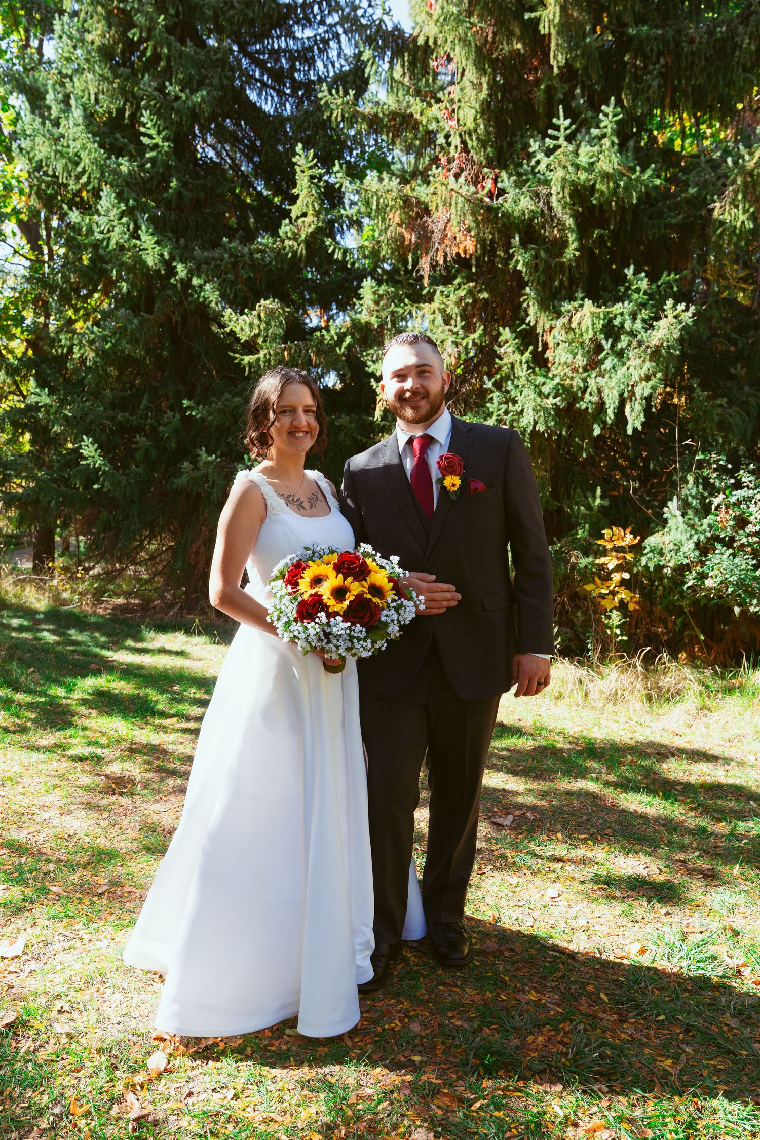 Outdoor wedding photos featuring couple with sunflower bouquet among green trees.