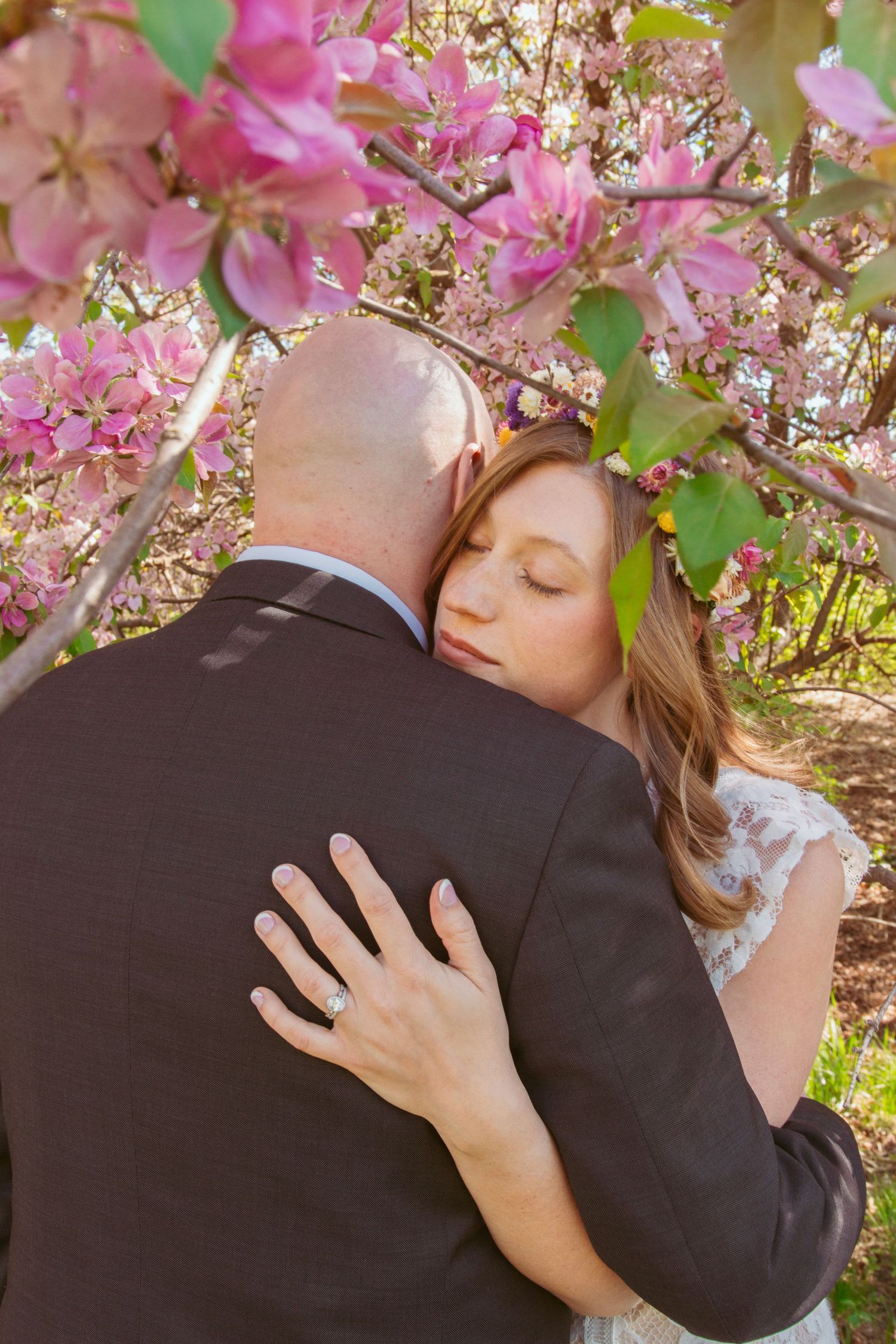 Tender moment captured under blooming pink cherry blossoms during a spring wedding.