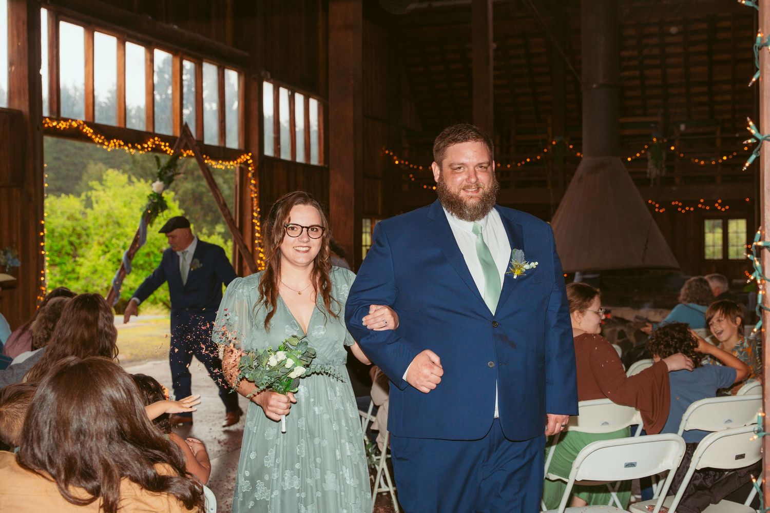 Wedding ceremony processional in a rustic barn venue with natural lighting and wooden interior.