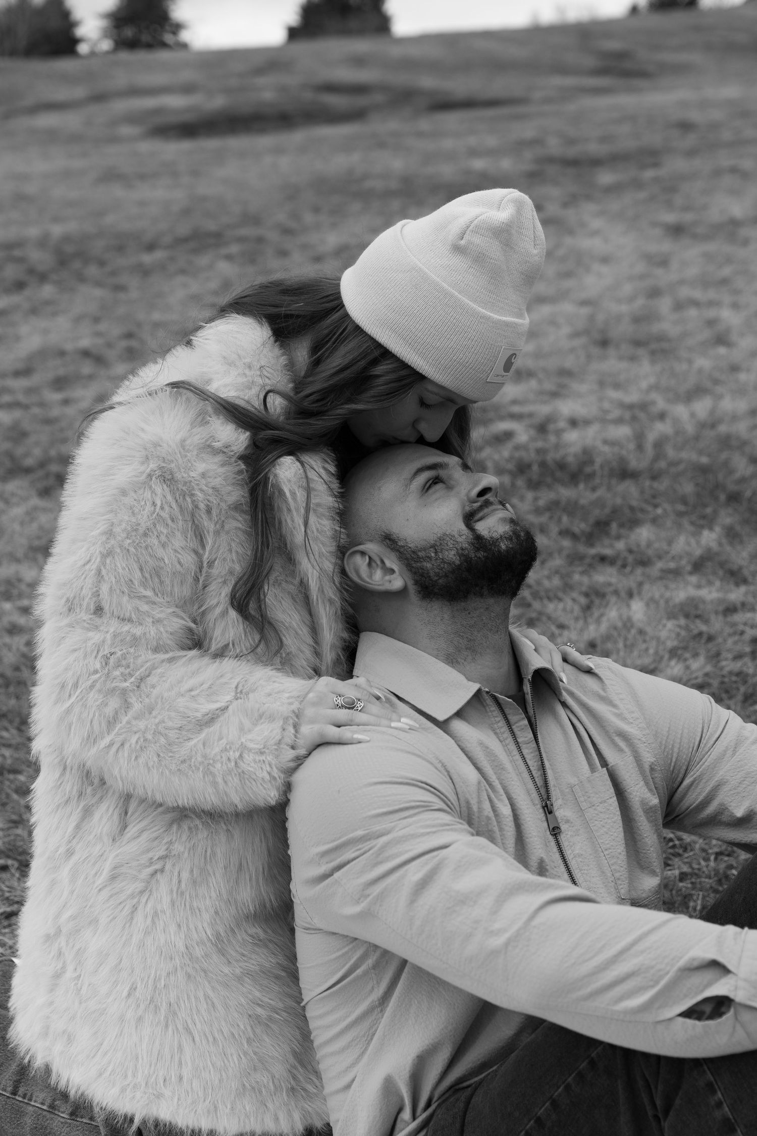 Black and white photo of couple sharing tender moments while sitting on grass.