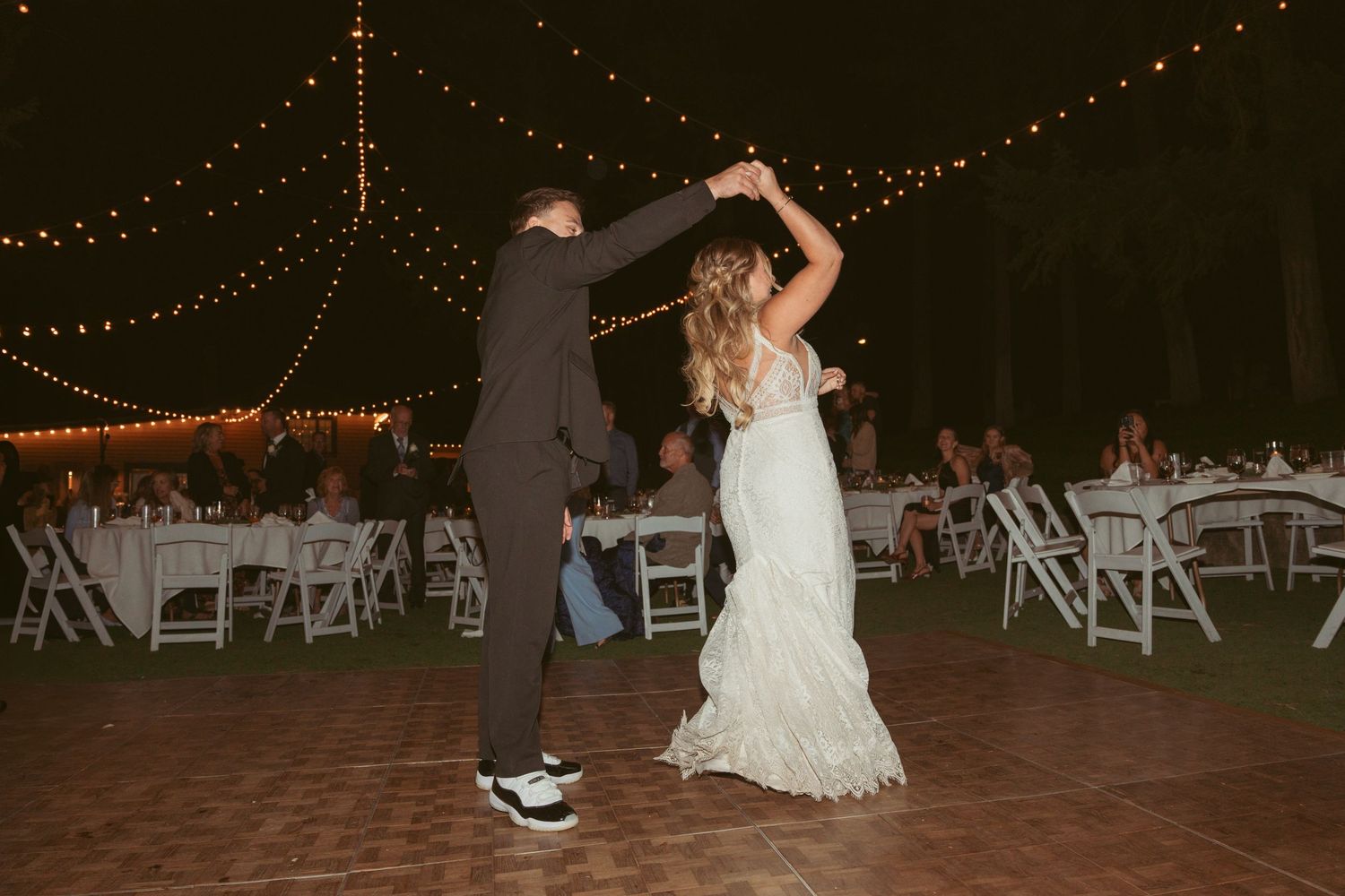 Wedding guests dance and celebrate on an outdoor patio decorated with twinkling string lights.