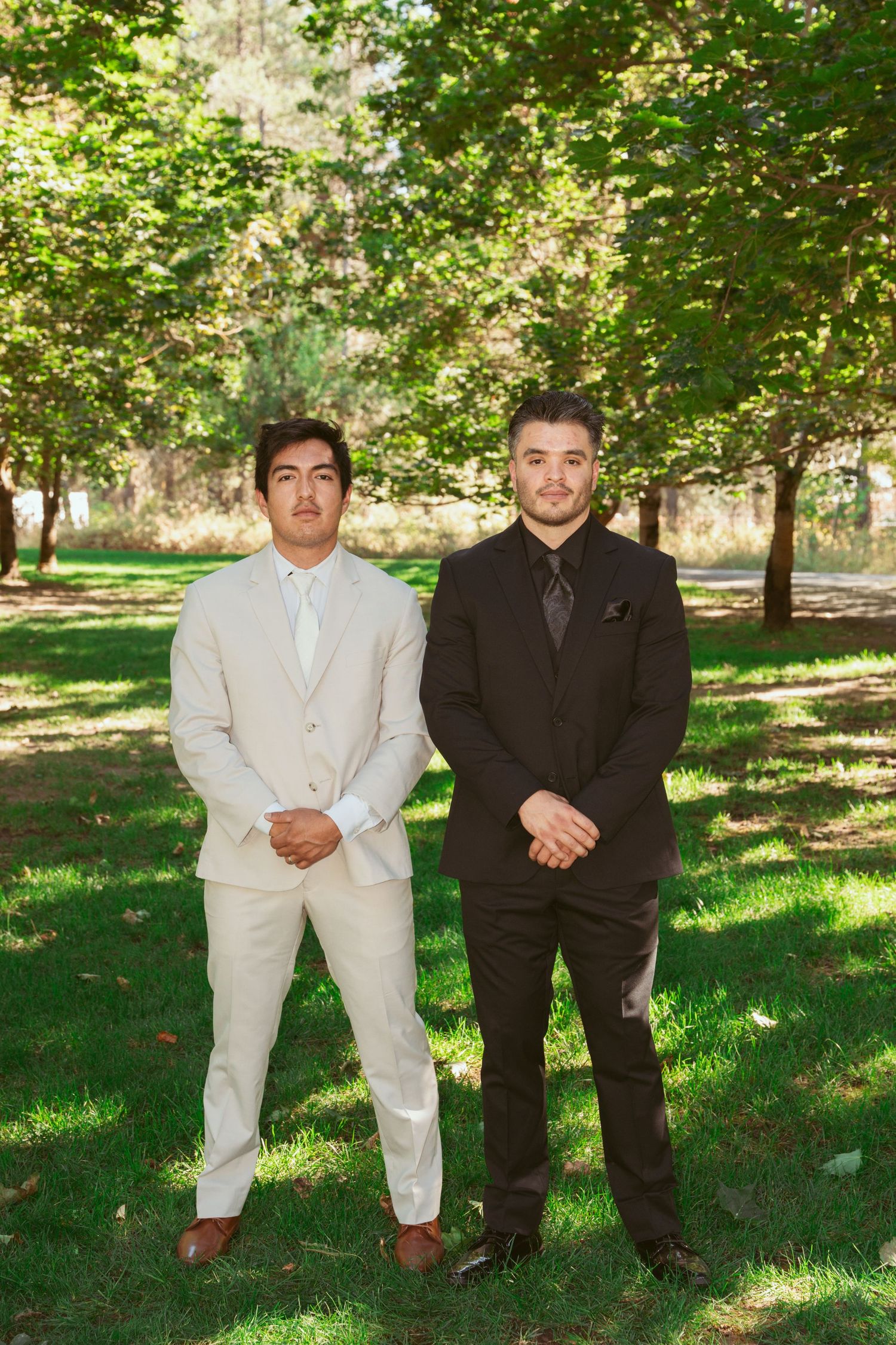 Groomsmen in contrasting black and cream suits pose on grass under trees.
