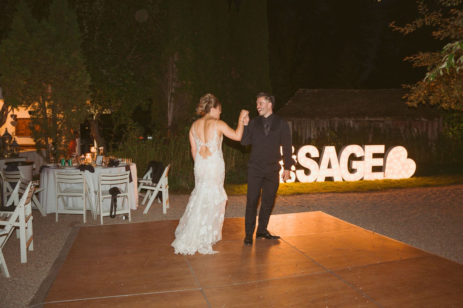 Romantic outdoor wedding reception with illuminated signage and guests enjoying the evening atmosphere.