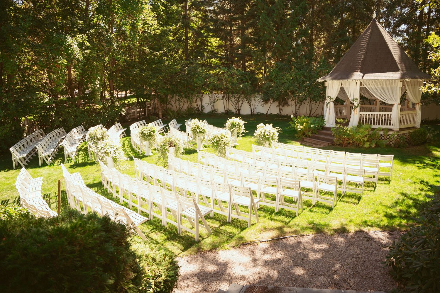 Rows of white chairs arranged in a curved pattern on a lawn leading to a decorated wedding gazebo.