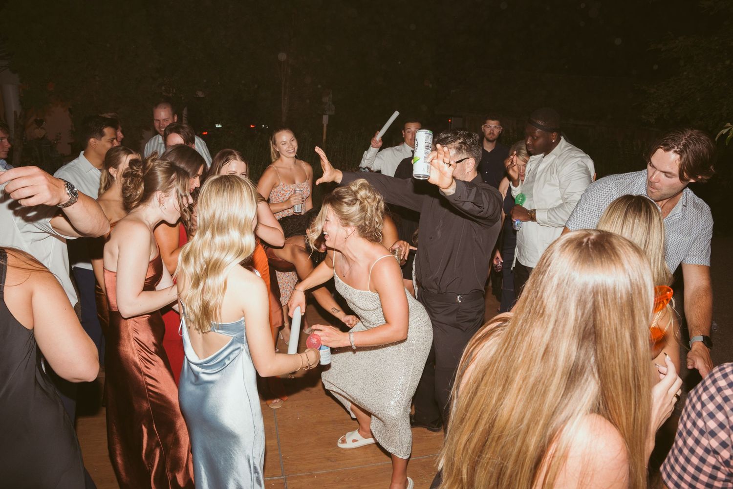 Energetic crowd dancing and celebrating at an outdoor evening wedding reception.