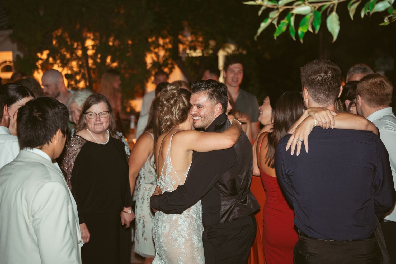 Crowd of party guests dancing and mingling at an evening outdoor celebration with string lights.