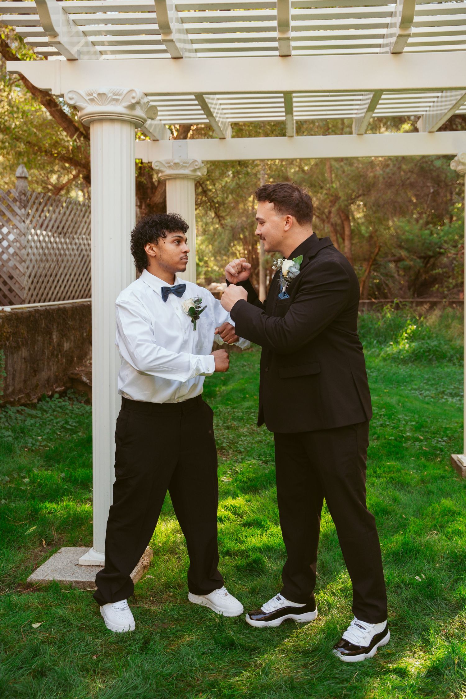 Two people in contrasting black and white outfits engage in a playful moment under a white garden pergola.
