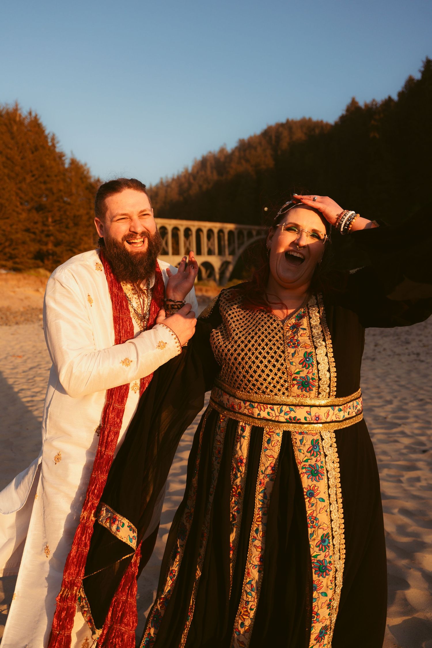 A candid moment of laughter between two people in historical costumes on a beach.