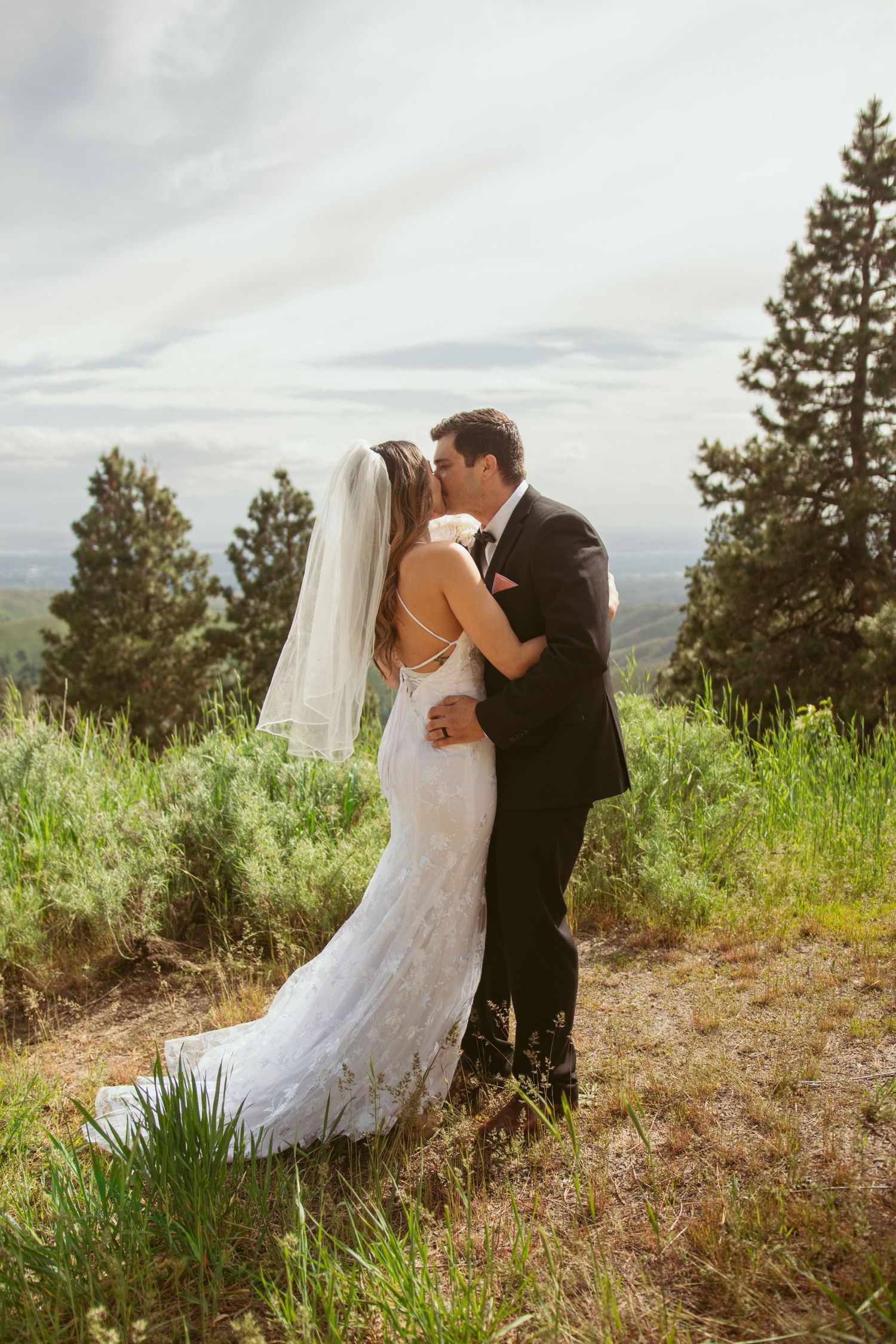 Newlyweds sharing their first kiss on a scenic mountain overlook.