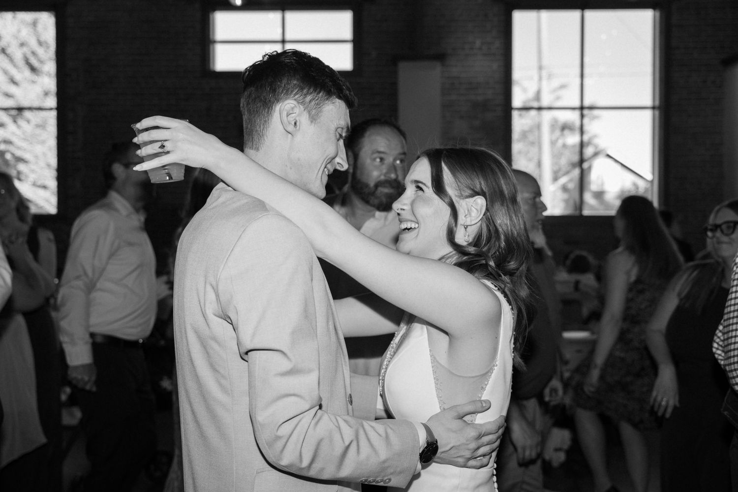 Black and white photo of couples dancing at a wedding reception in a rustic venue.