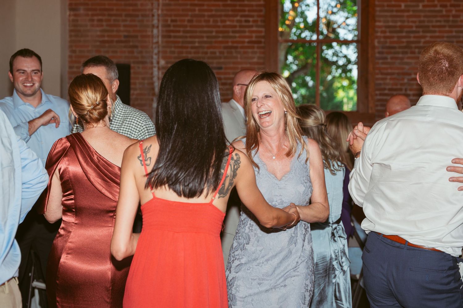 Wedding guests dance and laugh together during a reception celebration in a rustic venue.