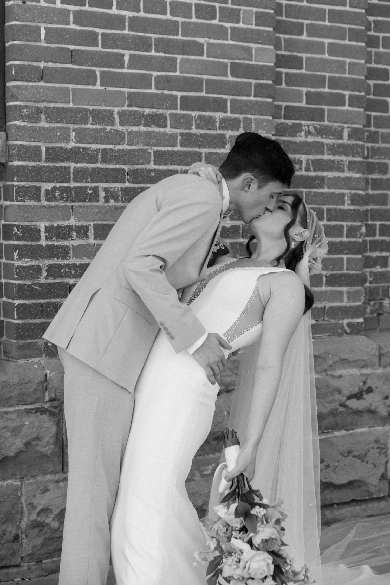 Black and white romantic wedding photo against brick wall backdrop.