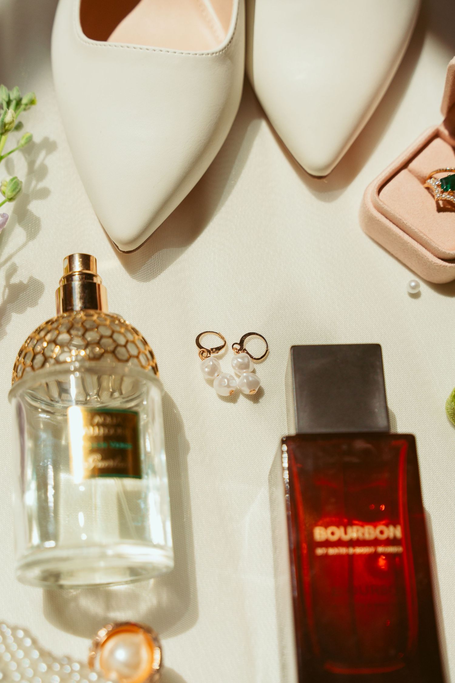 Wedding accessories including perfume bottles, white heels, jewelry, and ring boxes arranged on white surface.