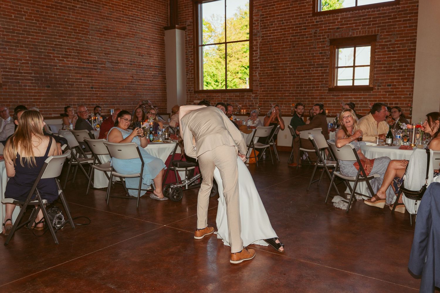 Wedding guests dance and celebrate in a rustic brick-walled venue with string lights overhead.