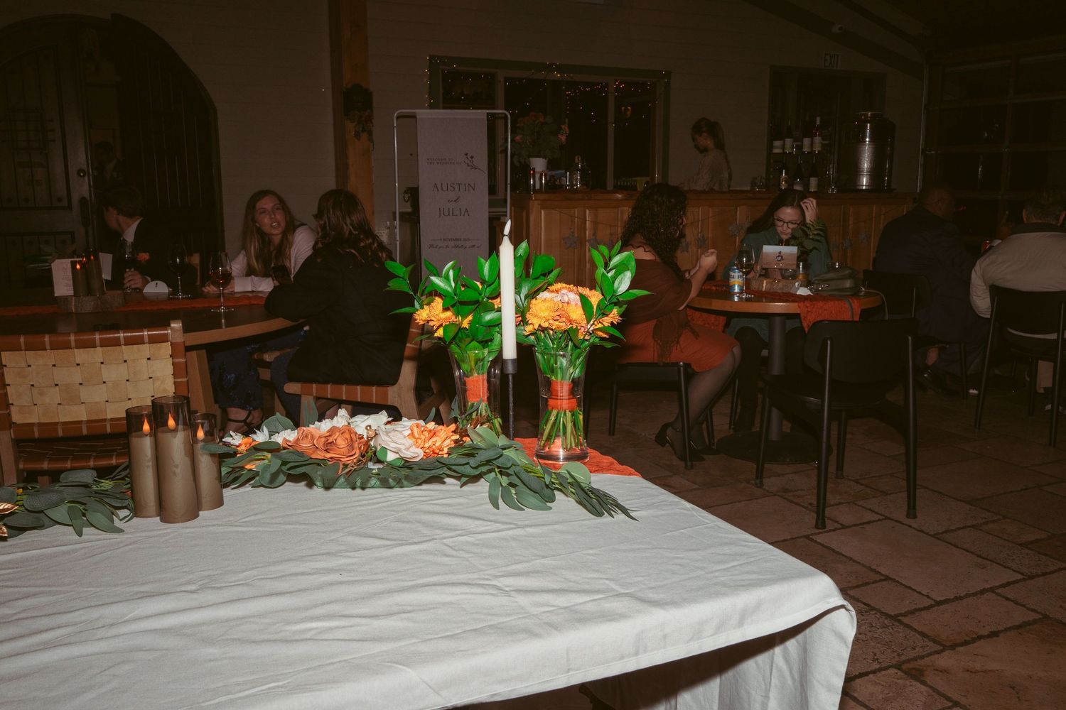 Elegant banquet table decorated with candles and greenery in a dimly lit indoor venue.