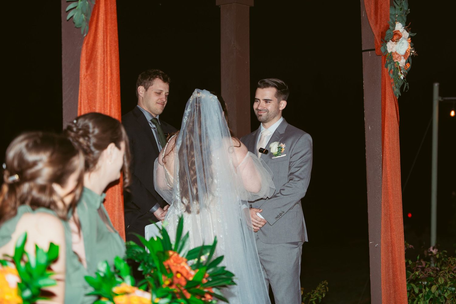 Outdoor evening wedding ceremony with orange draping and floral decorations on the pavilion.