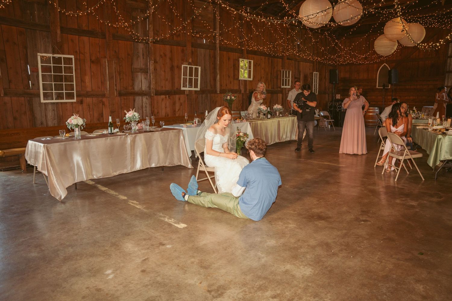 Wedding celebration in a rustic barn with string lights and paper lanterns overhead.