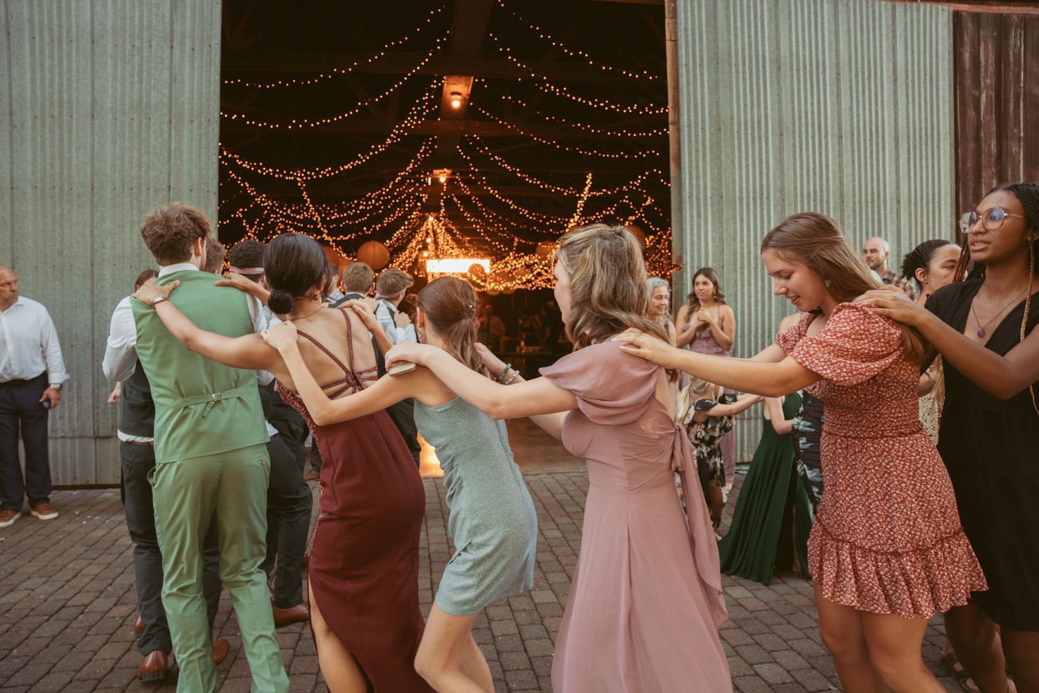Wedding party performs coordinated dance moves during outdoor evening celebration.