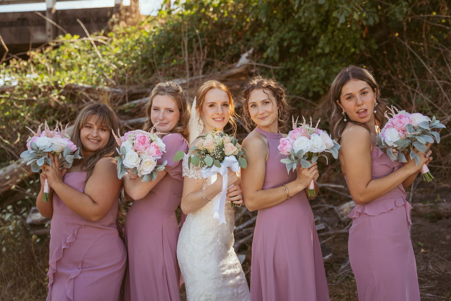 Bridal party creates fun photo sequence holding bouquets against rustic outdoor setting.