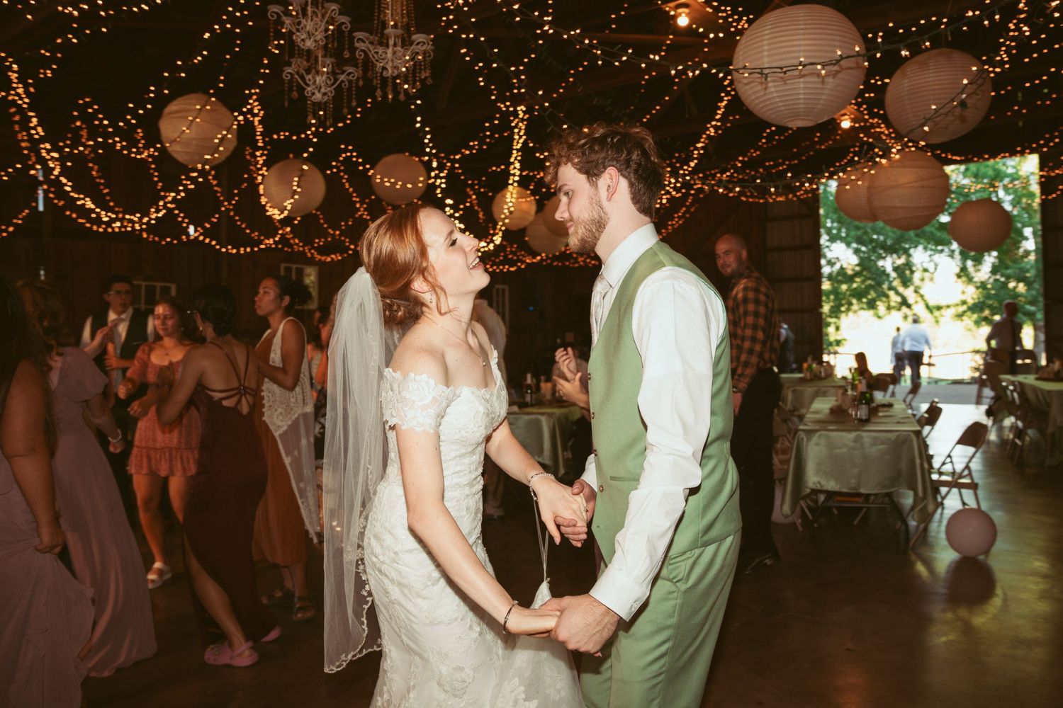 Couples dancing together during a romantic barn wedding reception with string light ambiance.
