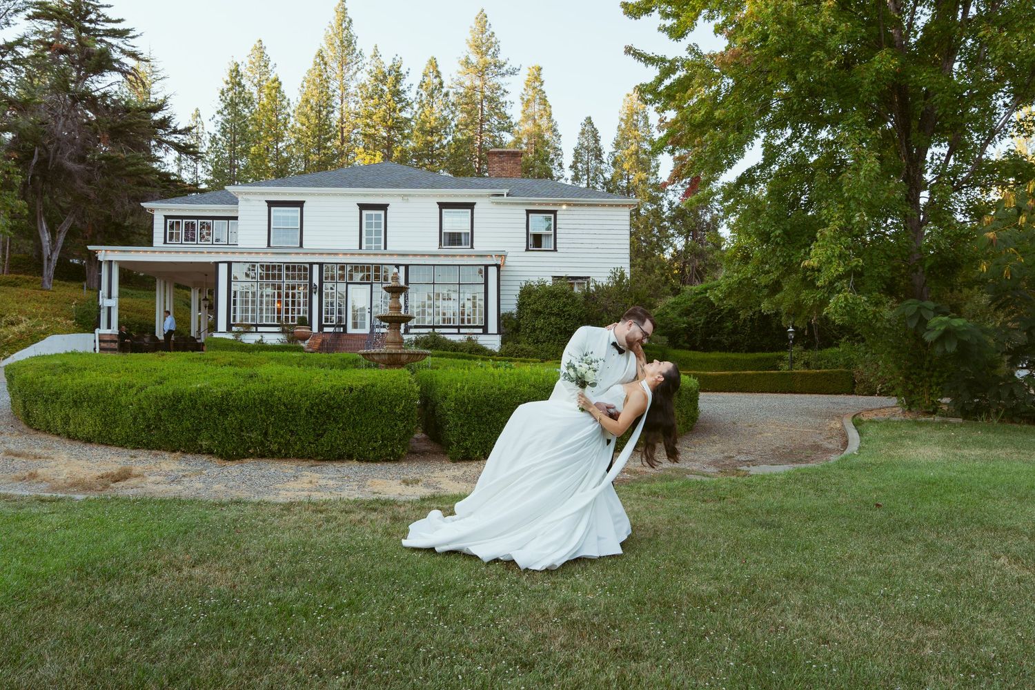 A wedding celebration on a sprawling lawn with a white house in the background.