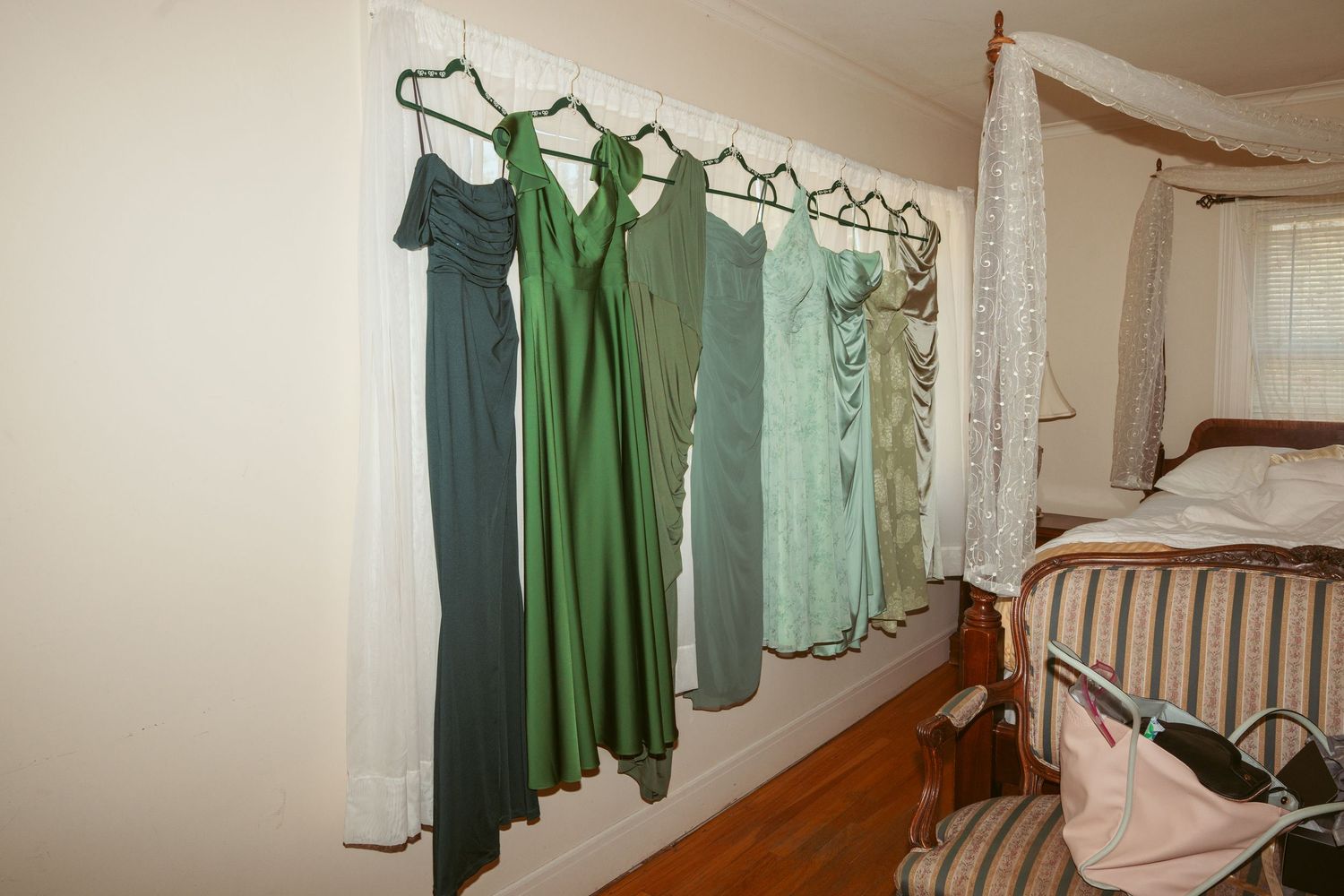 Elegant bridesmaid dresses in various shades of green and mint hanging on a wall in a bedroom.