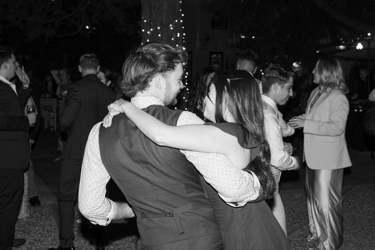 Couples dancing together at a dimly lit outdoor wedding reception.