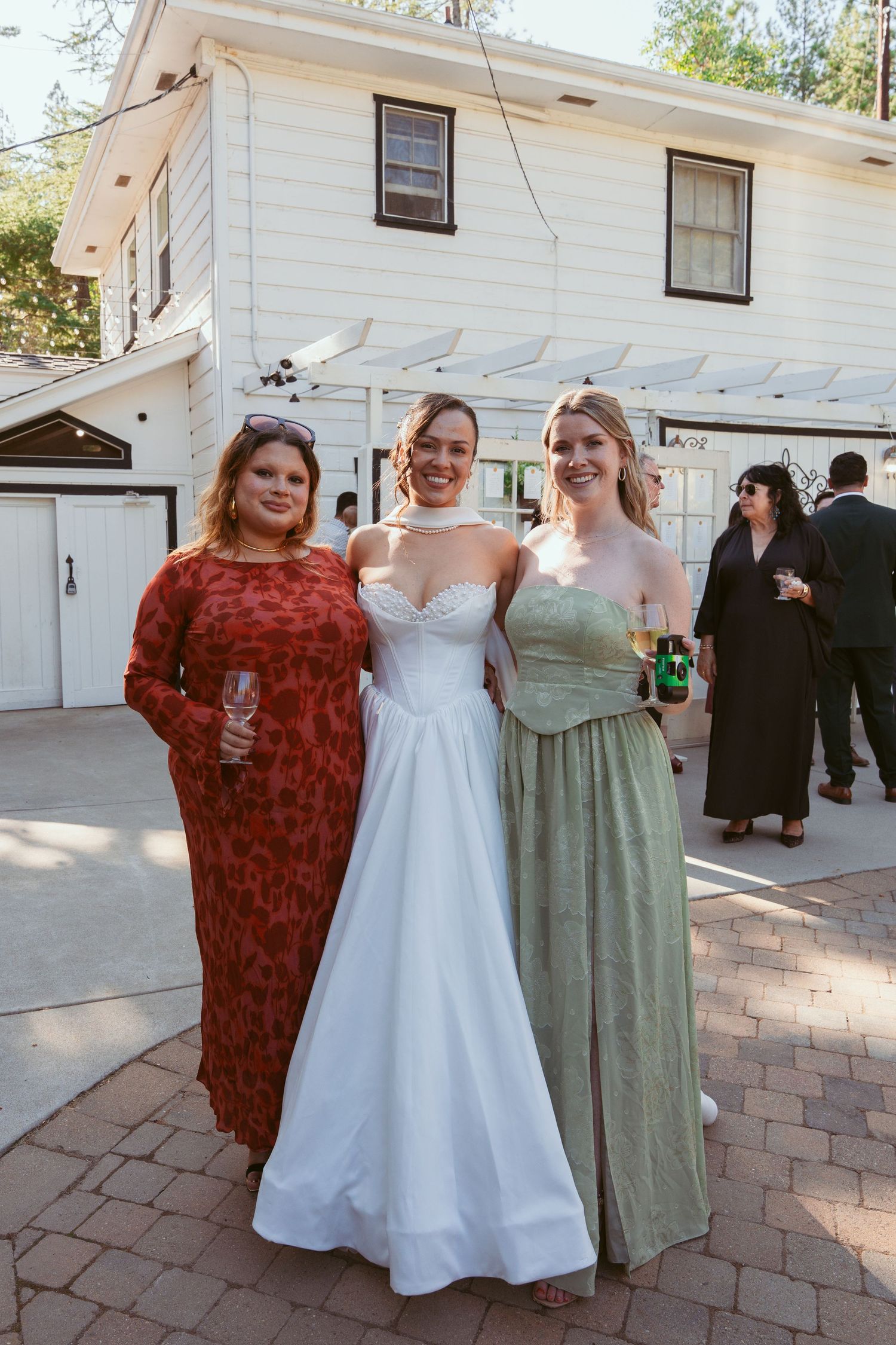 Wedding party posing together outside a white house wearing coordinated dresses in green and white.