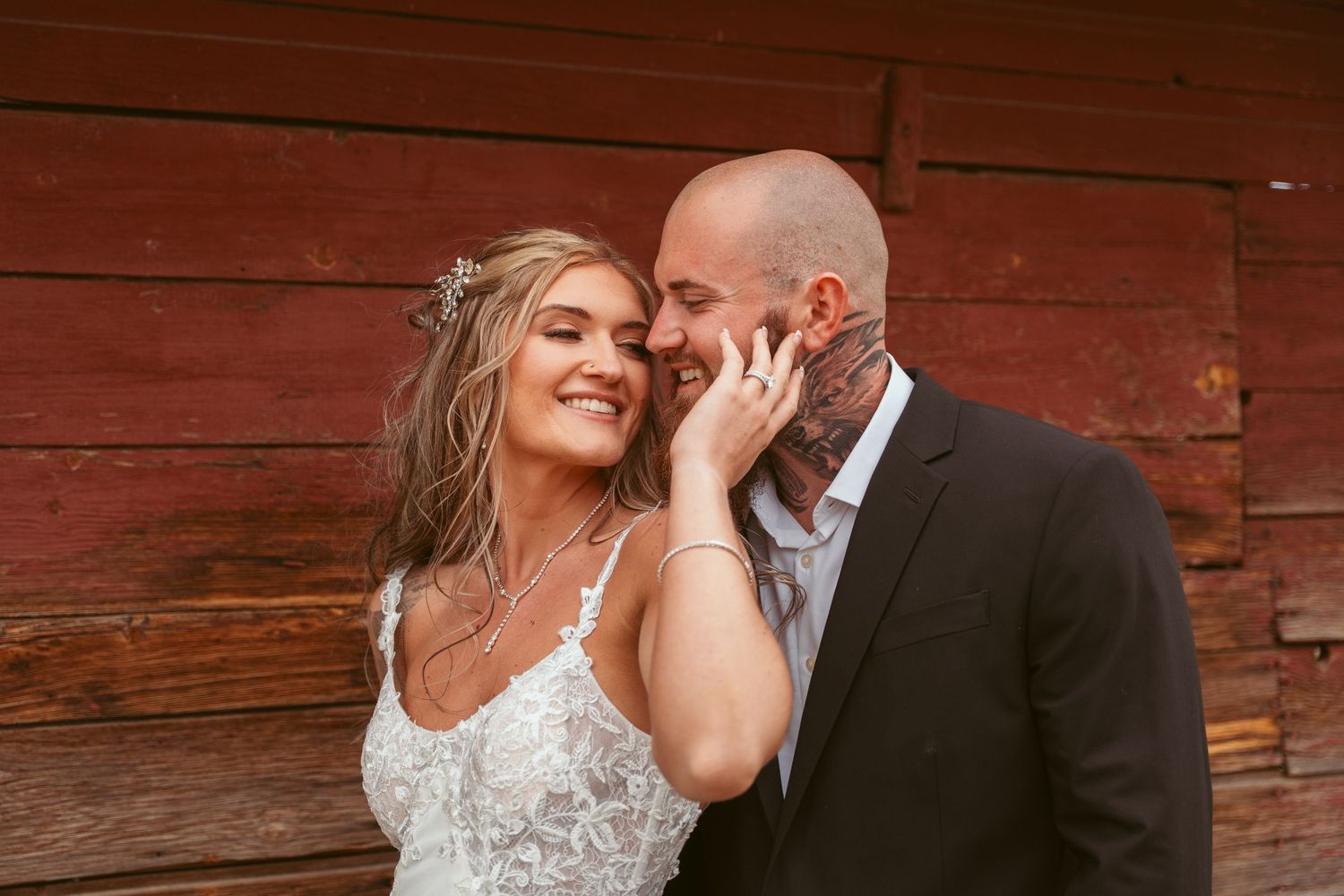 Couple shares joyful moment against rustic red barn wall.